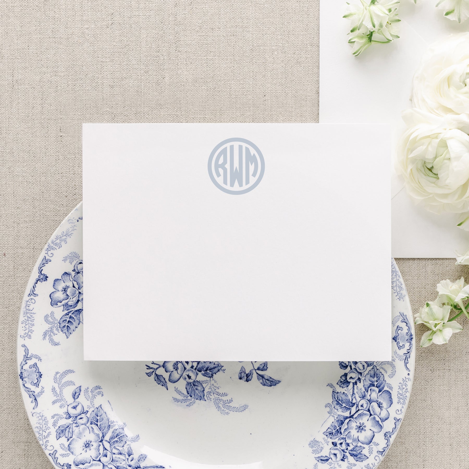Personalized circle monogram stationery in soft blue ink displayed on blue floral plate with white flowers by Swoon Paper Co.