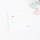 Personalized note card with blush heart pattern and one red accent heart, styled with pastel heart cookies on a white background.