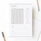 Personalized baby care log notepad with sections for feeding, sleep, diapers, and notes shown on white desk with pencils.