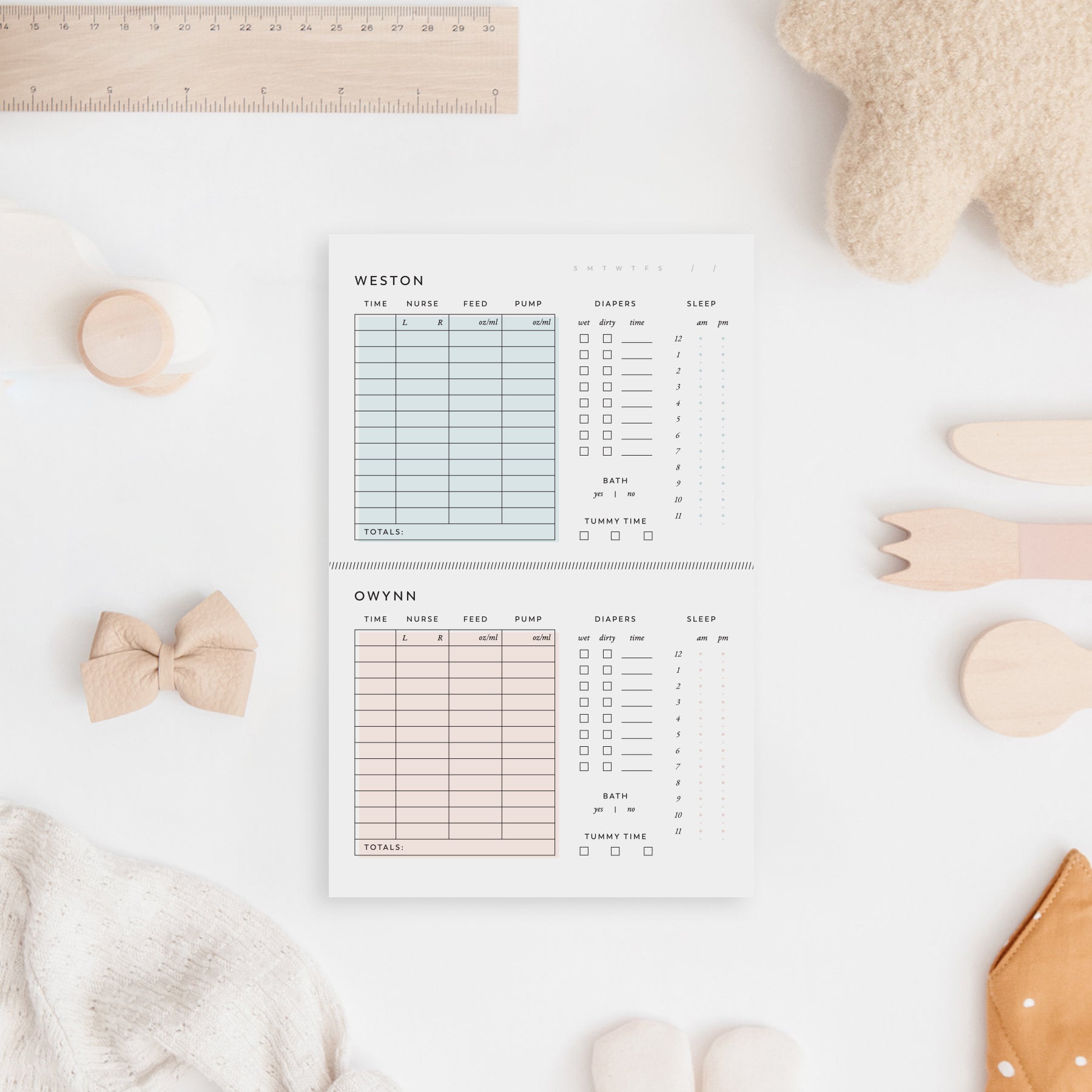 Twin baby daily log notepad with pastel blue and blush sections for tracking nursing, feeding, pumping, diaper changes, and sleep — styled on a soft neutral nursery background with baby toys and accessories.