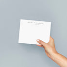 Personalized family stationery with elegant script font, shown held by hand against a soft dusty blue background.