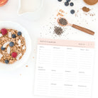 Styled image of personalized Weekly Market List Notepad in blush pink with breakfast ingredients, granola, and berries on a white kitchen counter